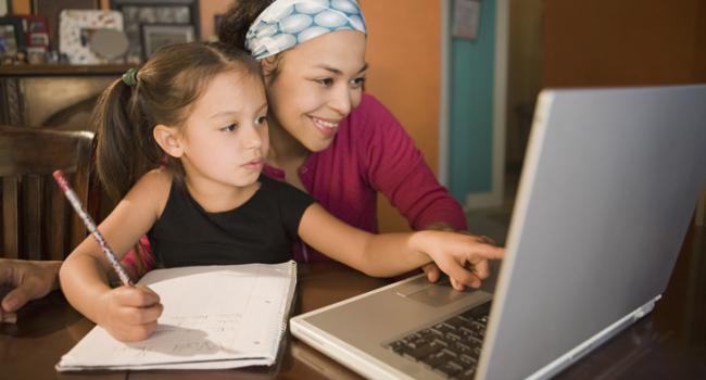 A woman and child are looking at a laptop screen and the girl is writing A woman and child are looking at a laptop screen and the girl is writing