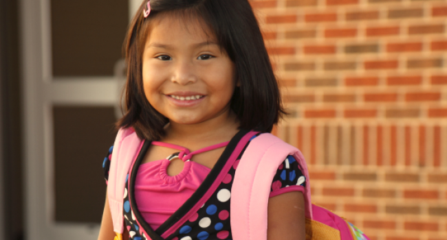 young girl smiling at camera and wearing a backpack
