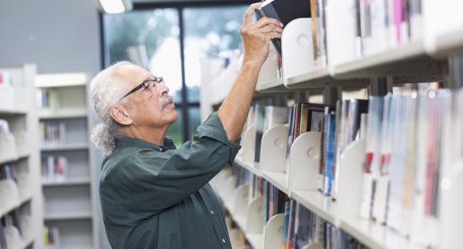 man putting book on a bookshelf man putting book on a bookshelf
