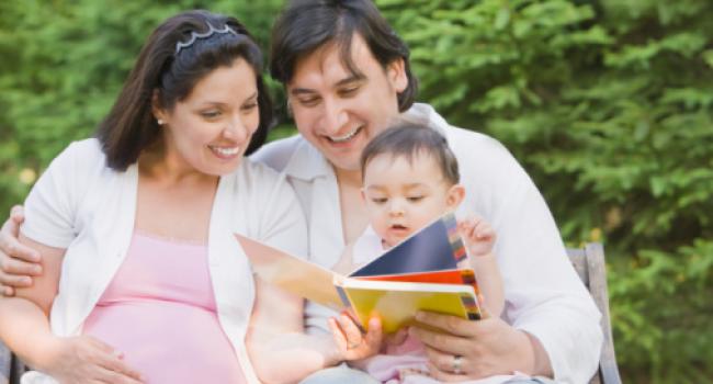 A pregnant woman, a man, and a baby all looking at a book